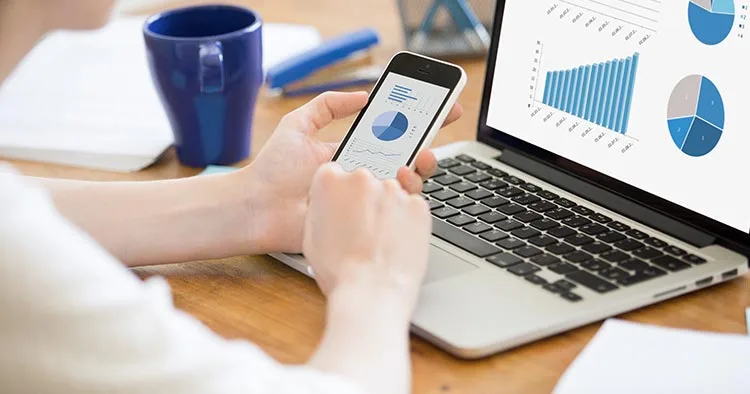 Marketer showing graphical presentations of digital marketing campaign results on laptop and mobile phone